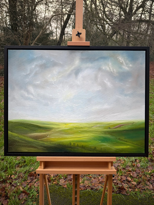 Framed oil painting of a peaceful green landscape with rolling hills and a bright, cloudy sky.